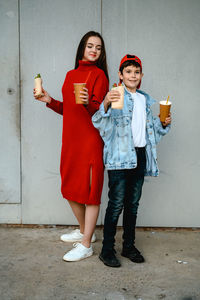 A girl in a red dress and a boy in a denim jacket are holding shawarma and a glass of coffee 
