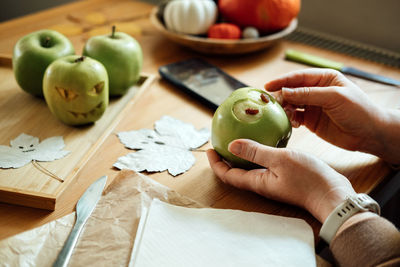 Halloween diy fruit ideas. female hands cutting out halloween green apple with creepy carved face