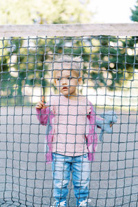 Portrait of boy standing against chainlink fence