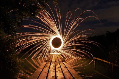 Illuminated wire wool spinning over lake at night