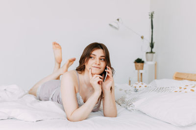 Beautiful girl talking on the phone using technology while lying in bed at home