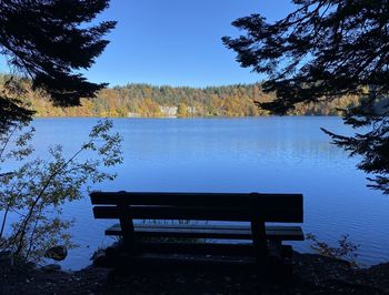 Empty bench by lake against clear blue sky