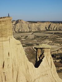 Woman standing on rock formation at landscape against sky