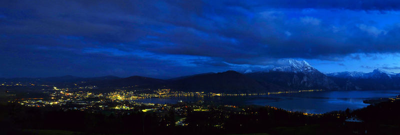 Illuminated city by lake against sky at night