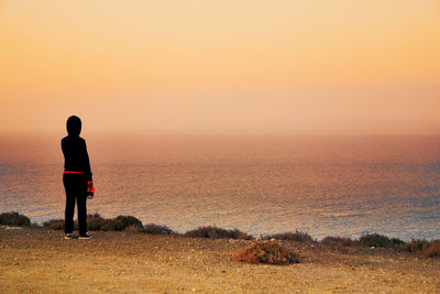 Rear view of man standing on shore during sunset