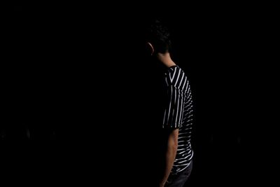 Side view of man standing against black background