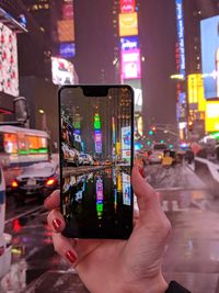 Midsection of person photographing illuminated mobile phone in city