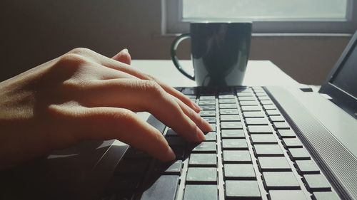 Cropped hand using laptop by coffee cup at home