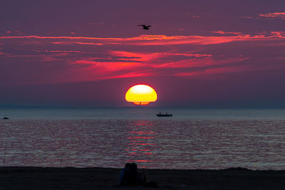 The golden sun rising above lighthouse and fisherman in the ocean.