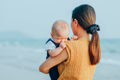 Mother and daughter by sea against clear sky