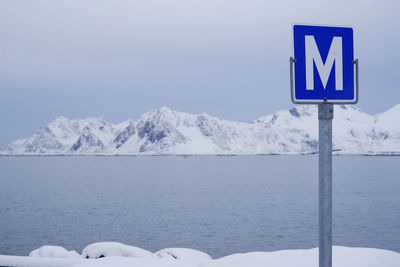 Road sign on snowcapped mountain against sky