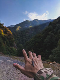 Cropped hand of man with lizard against mountain range