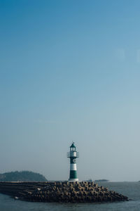 Lighthouse by sea against clear sky