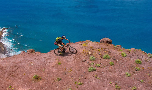 High angle view of man riding bicycle by cliff against sea