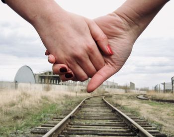 Midsection of person on railroad tracks against sky