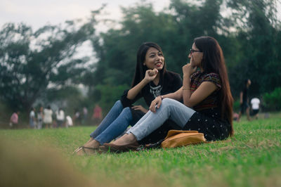 Smiling friends sitting on field against sky