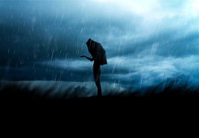 Side view of silhouette woman holding umbrella against cloudy sky during rainy season at night