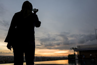 Rear view of woman standing against sky during sunset