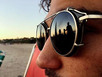 Cropped image of man wearing retro sunglasses at beach during sunset