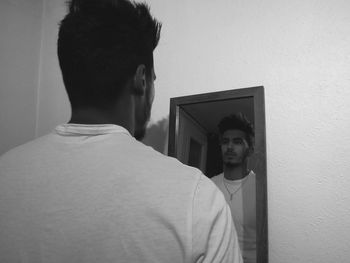 Rear view of man standing against wall at home