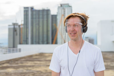 Portrait of smiling young man standing against buildings