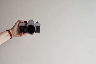 Cropped hand holding camera against wall