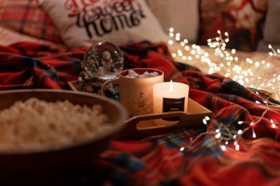 Cup of cocoa and marshmallows and burning candle on tray on red plaid in bed and a garland
