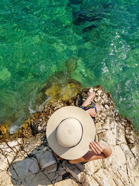 High angle view of woman on rock at beach. summer, lifestyle, sea, hat, overhead.