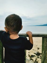 Rear view of boy looking at sea against sky