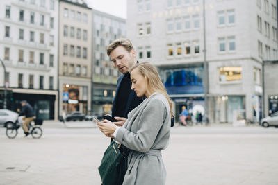 Side view of businesswoman using phone while walking by colleague in city