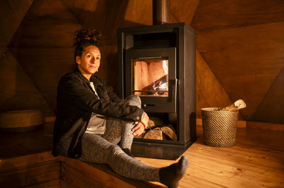 Woman warming herself sitting near a fireplace.