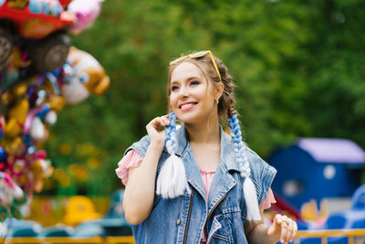 Happy caucasian woman with blue pigtails in a denim vest in an amusement park enjoying the weekend