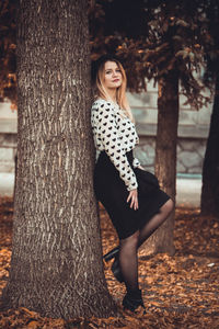 Portrait of beautiful young woman against tree trunk in forest