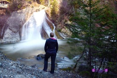 Rear view of man looking at waterfall in forest