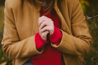 Midsection of woman with hands clasped sitting on field