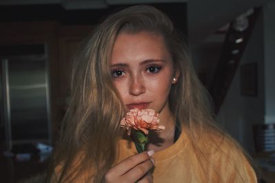 Close-up portrait of young woman holding carnation while standing at home