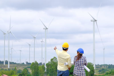 People on wind turbines against sky