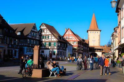 People walking in city against blue sky