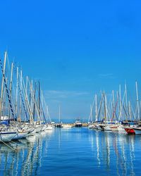 Sailboats moored in harbor against clear blue sky