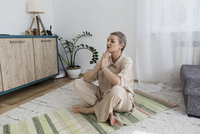 Mature woman with sitting on rug at home meditating