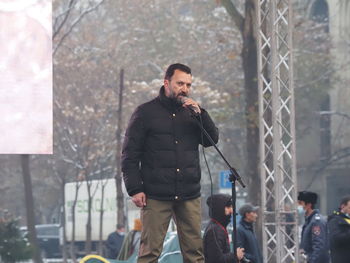 Young man using mobile phone while standing against built structure