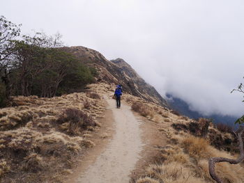 Rear view of man walking on mountain against sky