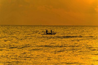 Silhouette men in sea against sky during sunset