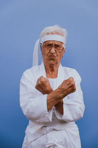 Portrait of senior woman doing karate against blue background