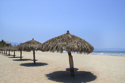 Thatched roof umbrellas at beach against clear sky on sunny day