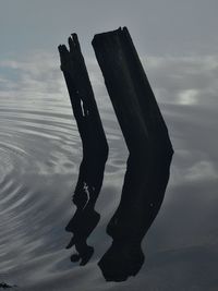 Silhouette of wooden post in sea against sky