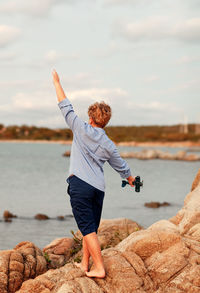 Rear view of woman standing on rock by sea