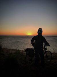 Rear view of silhouette man on beach against sky during sunset