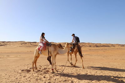 Man and woman sitting on camel in desert