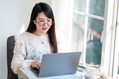 Young woman using phone while sitting on table